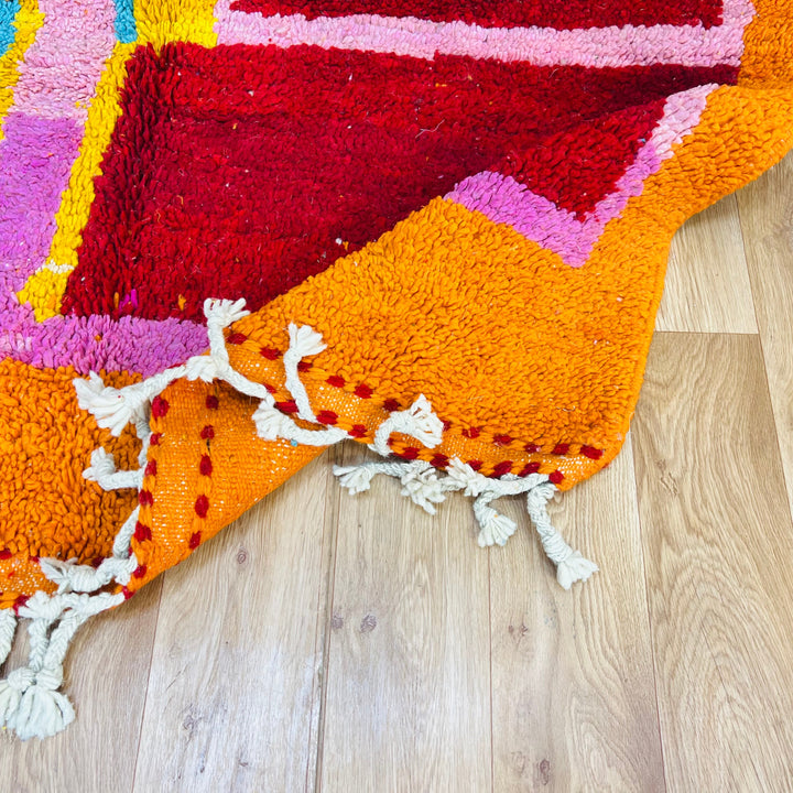 Vintage Moroccan rug in vibrant orange, red, and pink abstract design on a wooden floor. Handcrafted Berber wool area rug.
