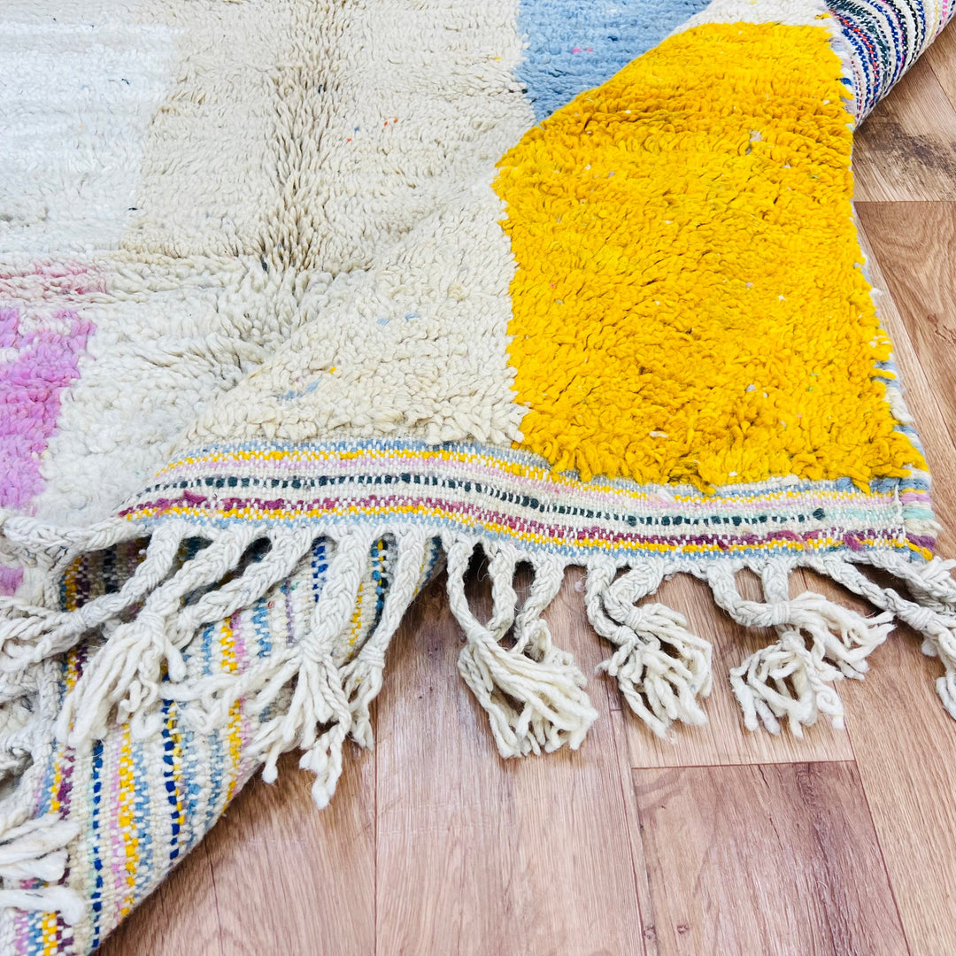 Colorful vintage Moroccan rug with geometric patterns in pink, yellow, and blue, showcasing traditional Berber craftsmanship on a wooden floor.