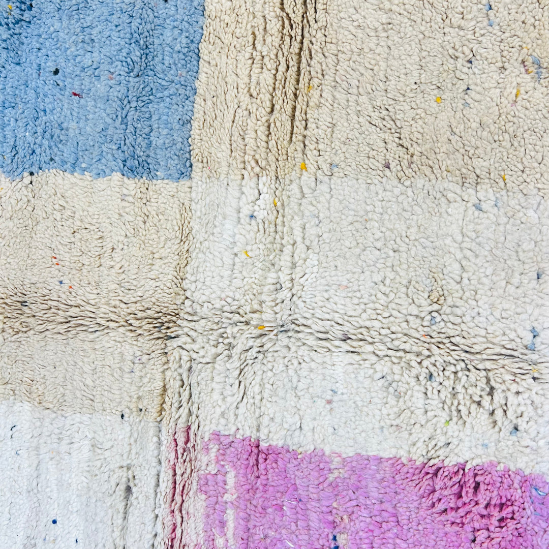 Close-up texture of a vintage Moroccan rug with geometric patterns in blue, pink, and cream. Handmade by Berber artisans.