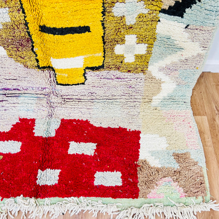Vintage Moroccan Berber rug with abstract tribal motifs in mustard yellow, red, pink, blue, black, and ivory on wooden floor. Rug 428.