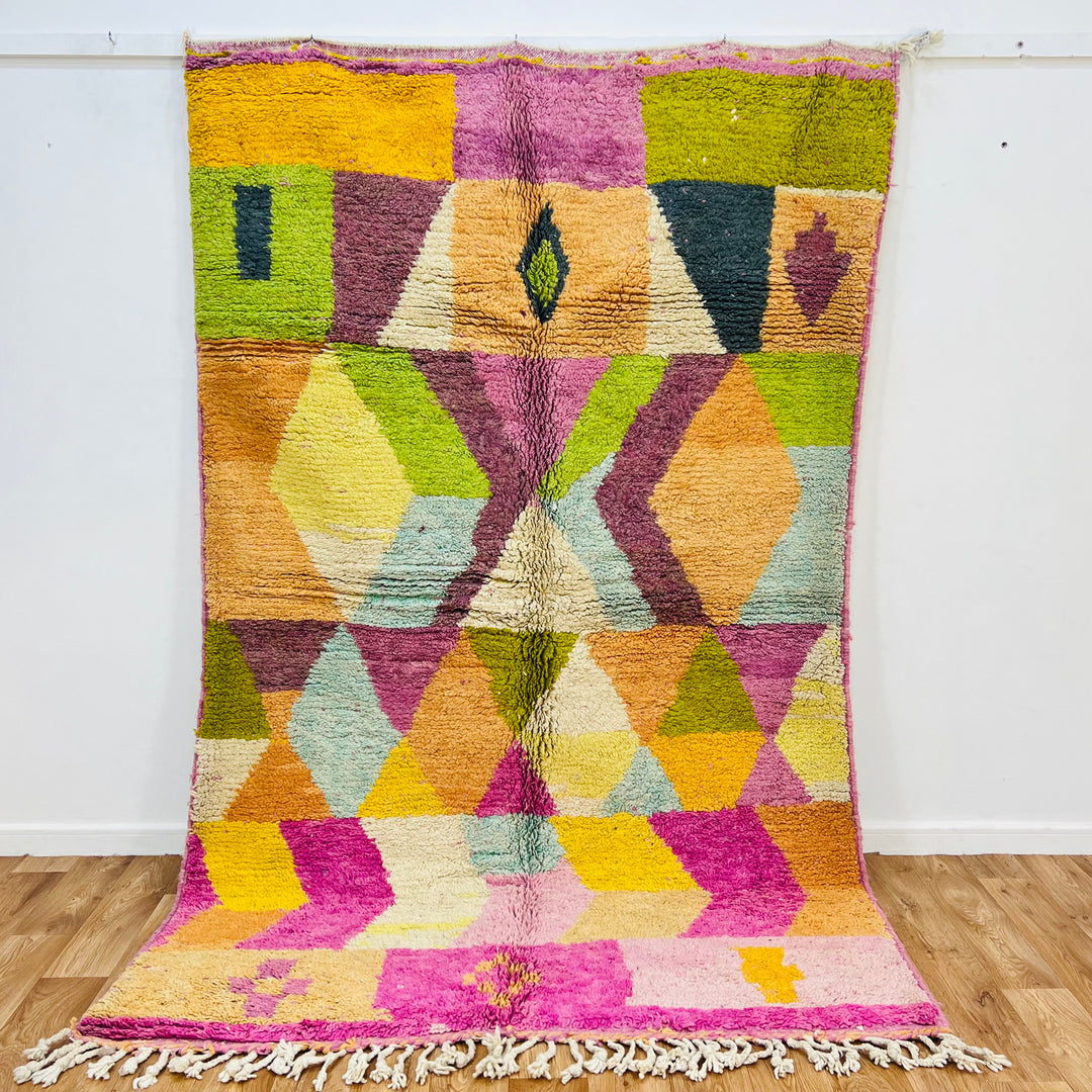 Colorful geometric Moroccan wool rug with earthy tones, handwoven by Berber artisans, featuring bold patterns and tassels.