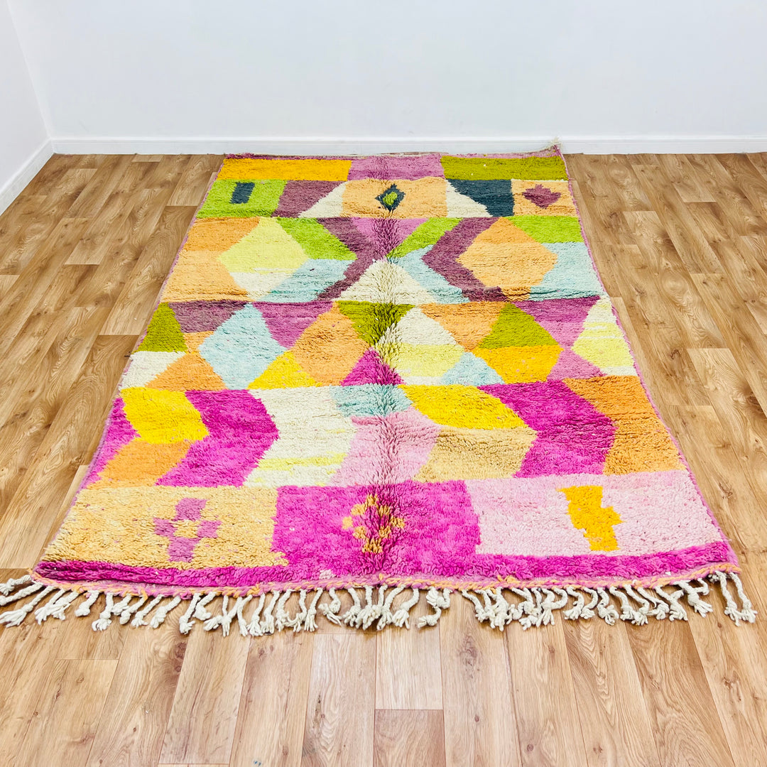 Colorful geometric Moroccan wool rug with bright pink, ochre, olive, and black diamond patterns and tassels. Vintage Berber style.