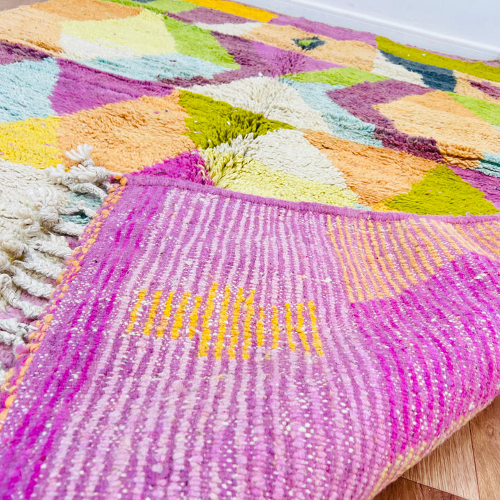 Colorful geometric Moroccan wool rug with pink base and tassels, featuring ochre, olive, terracotta, and mustard diamond patterns.