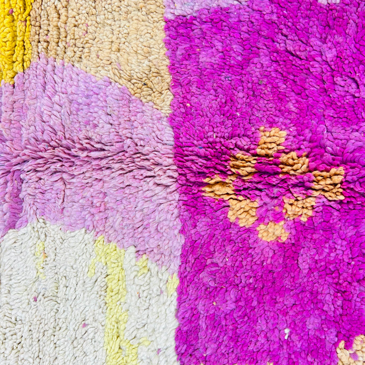 Close-up of a colorful geometric Moroccan wool rug with vibrant pink, yellow, and cream patterns, showcasing intricate handwoven texture.