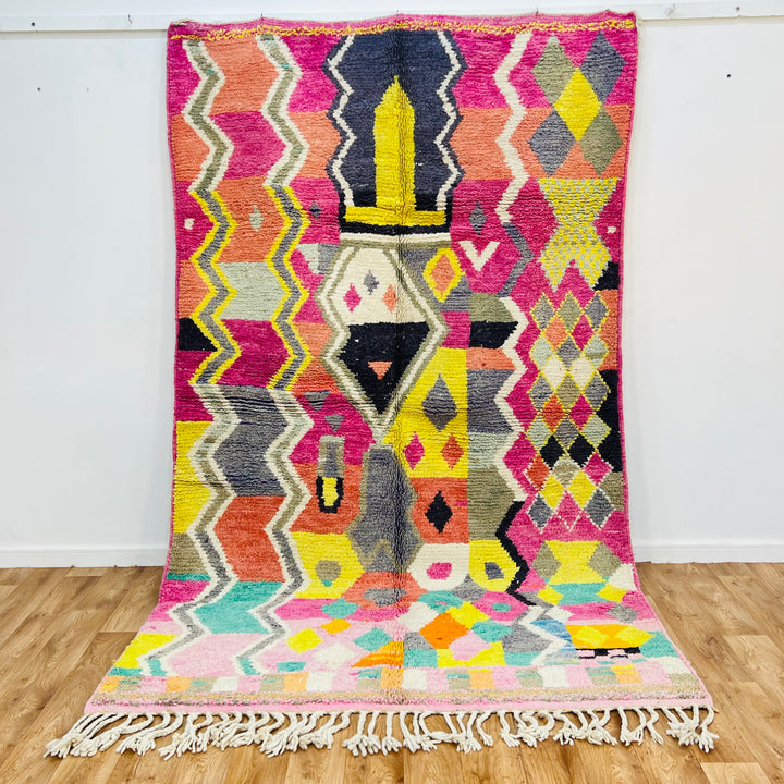 Colorful Moroccan Berber rug with pink, yellow, coral, teal patterns, tribal symbols, and zigzag lines, handmade in Morocco.