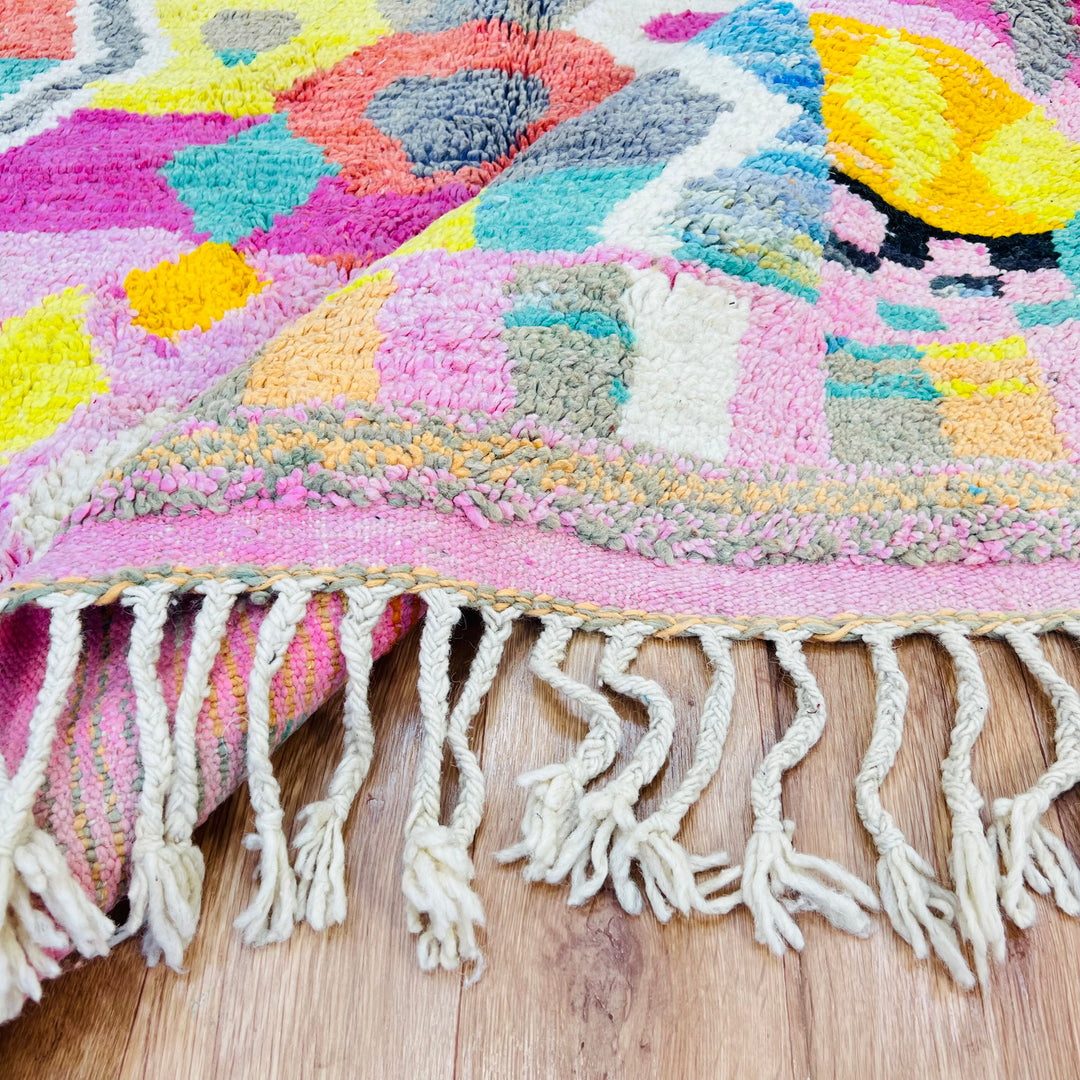 Vibrant Moroccan Berber rug with pink, yellow, and teal tribal patterns showcasing traditional handwoven designs on a wooden floor.