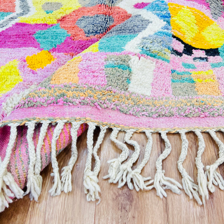 Vibrant Moroccan Berber rug with pink, yellow, and teal tribal patterns showcasing traditional handwoven designs on a wooden floor.