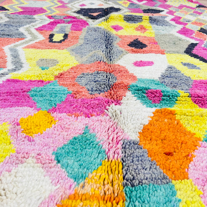 Colorful Moroccan Berber rug with pink, yellow, black, coral, and teal patterns, showcasing tribal symbols. Handmade in Morocco.