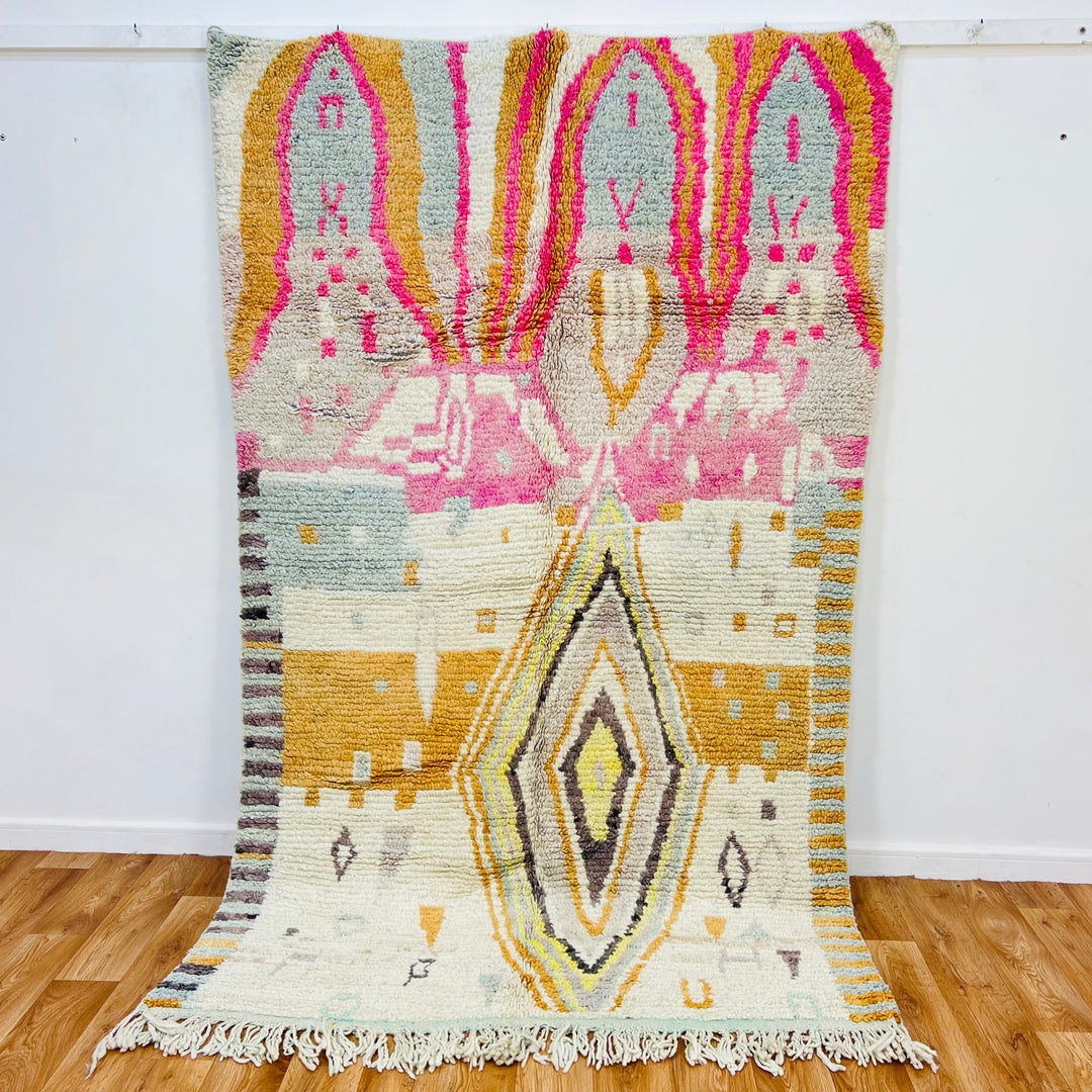Vintage Moroccan wool rug with central diamond and pink, gold, gray motifs, 8x5 ft, handwoven in Atlas Mountains. Moroccan decor.