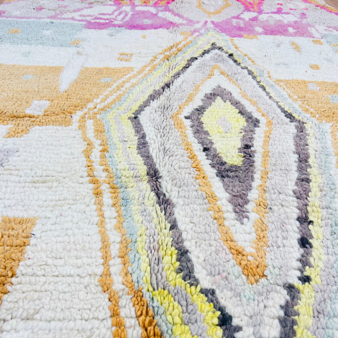 Close-up of a vintage Moroccan rug with pastel diamond pattern, featuring pink, gold, and gray motifs; handmade in the Atlas Mountains.