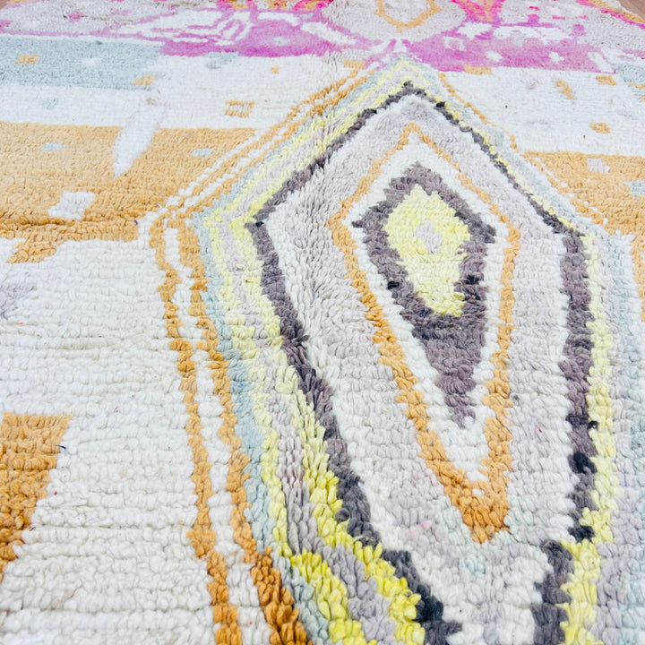 Close-up of a vintage Moroccan rug with pastel diamond pattern, featuring pink, gold, and gray motifs; handmade in the Atlas Mountains.