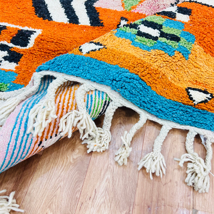 Colorful Moroccan wool rug with Berber diamond motifs, hot pink, orange, sky blue, and ivory tones, 254 x 150 cm.
