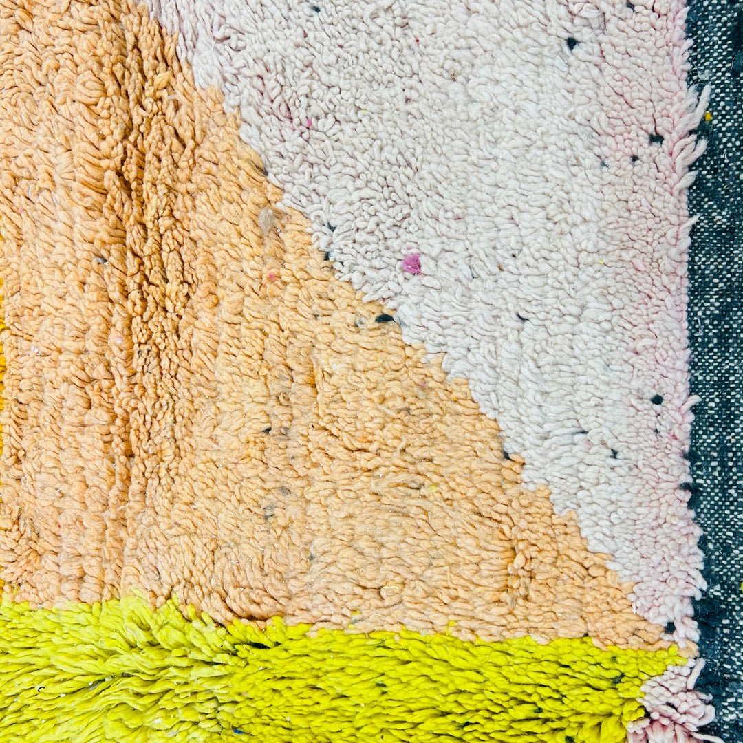 Close-up of a vintage abstract Moroccan wool rug with vibrant pink, blue, yellow, orange, and cream geometric design.