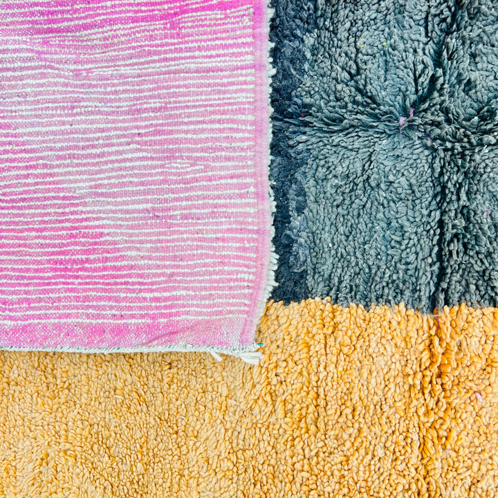 Close-up of a vintage Moroccan color block rug showcasing pink, black, and yellow wool textures. Traditional Berber craftsmanship.
