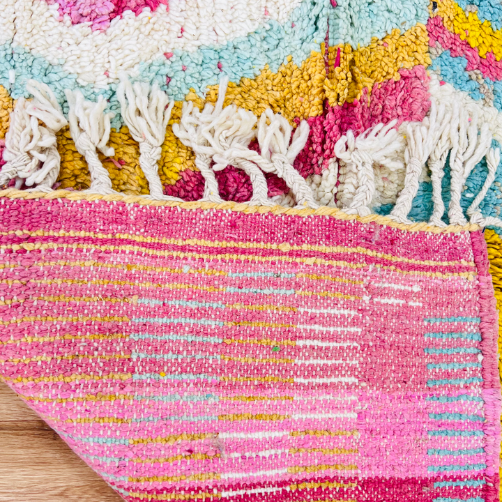 Colorful vintage Moroccan rug with pink, yellow, and blue patterns, showcasing traditional Berber designs and fringed edges.