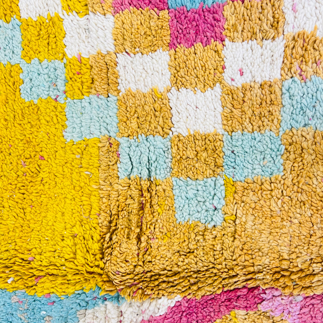Close-up of a vintage Moroccan rug with bold tribal abstract design in yellow, pink, and blue, featuring geometric patterns.