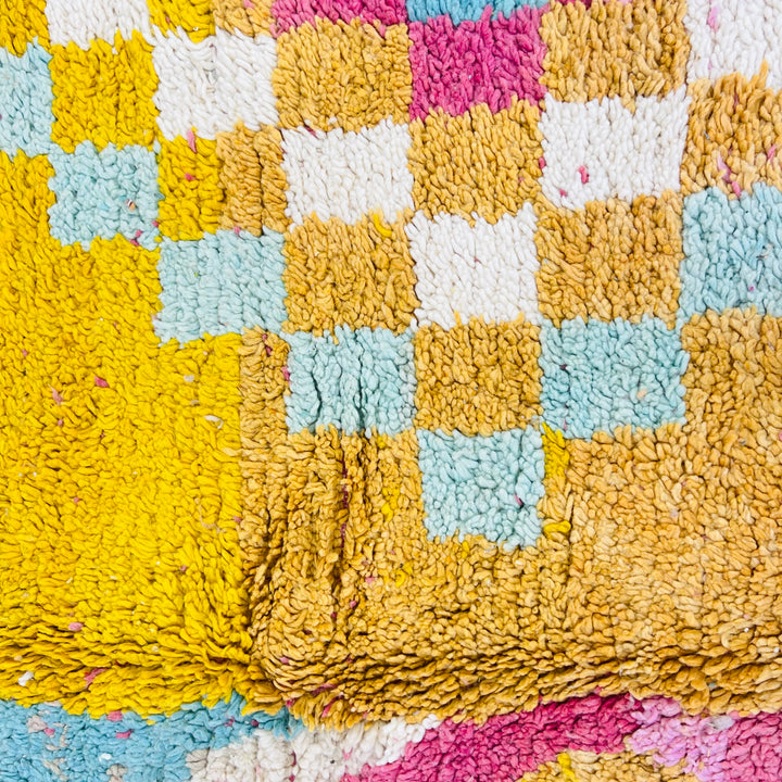 Close-up of a vintage Moroccan rug with bold tribal abstract design in yellow, pink, and blue, featuring geometric patterns.
