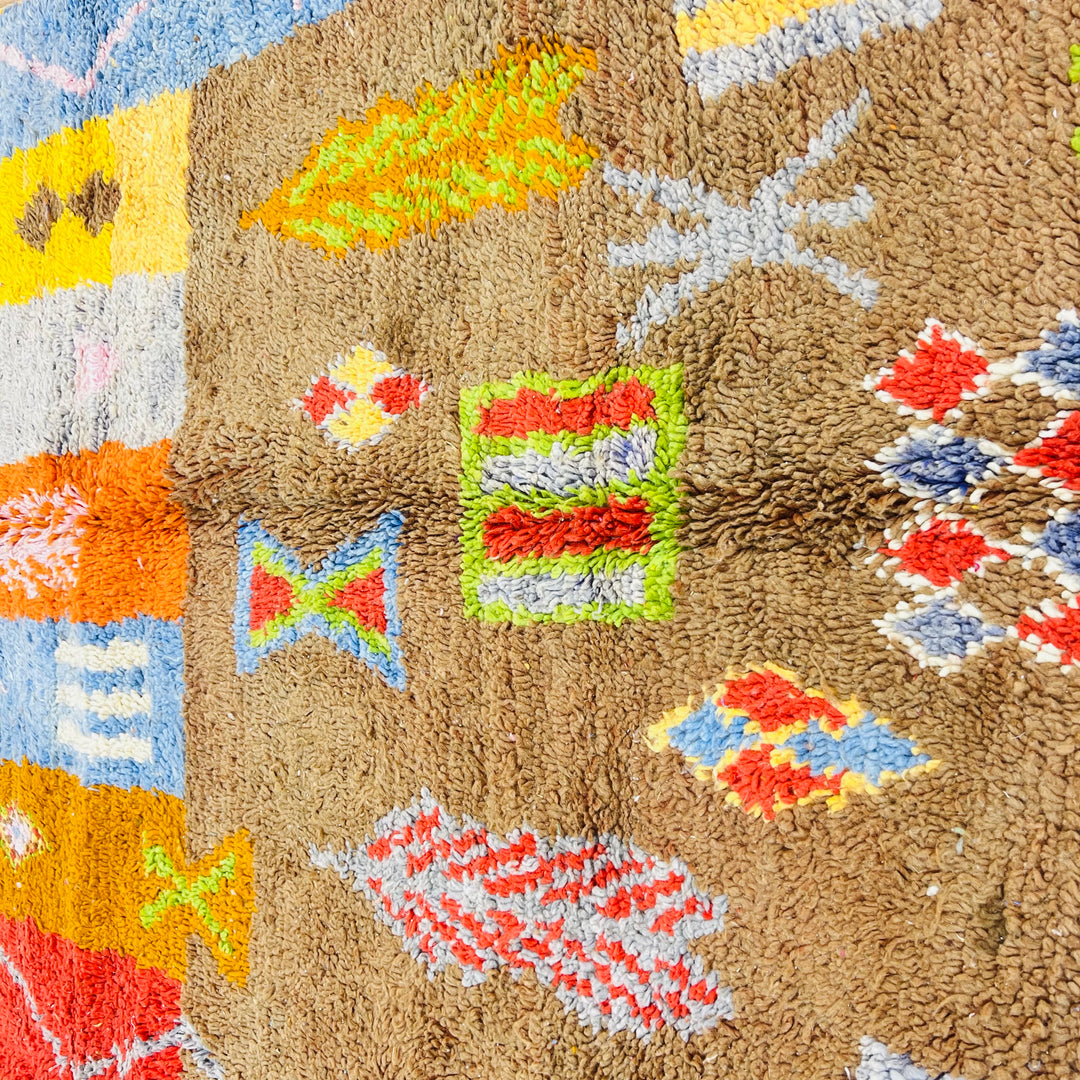 Handmade vintage Moroccan rug with colorful Berber symbols and motifs, featuring earthy tones of brown, red, yellow, and blue.
