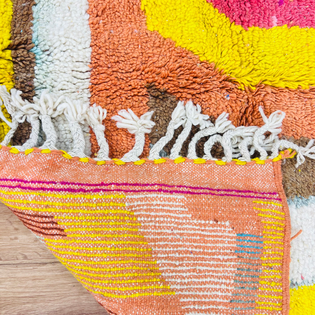 Close-up of colorful abstract Moroccan wool rug with geometric patterns and fringe, showcasing vibrant magenta, turquoise, and orange hues.