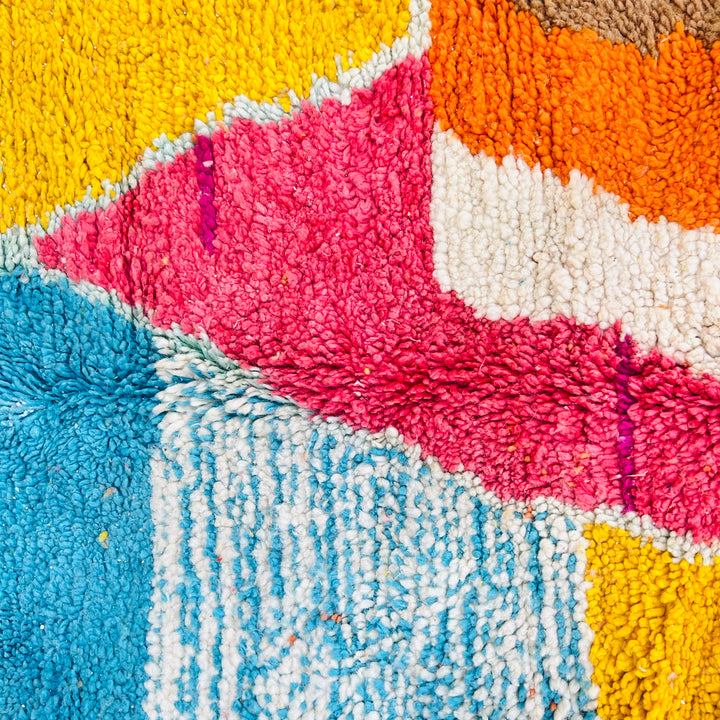 Colorful abstract Moroccan rug with geometric patterns in magenta, turquoise, and yellow shades for home decor.