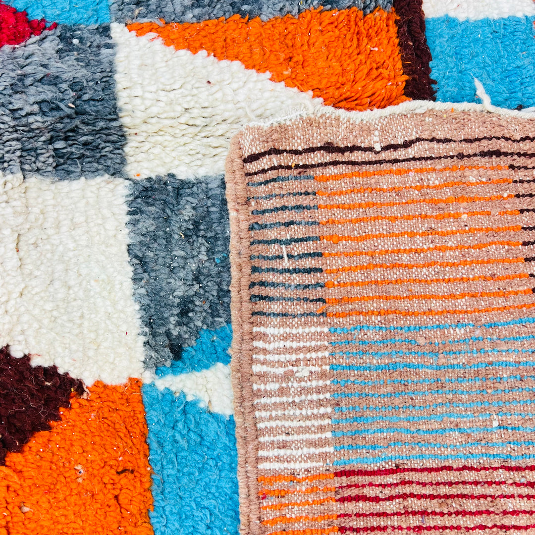 Close-up of a vintage Moroccan rug with bold geometric designs in burnt orange, sky blue, and cream, showcasing traditional Berber weaving.