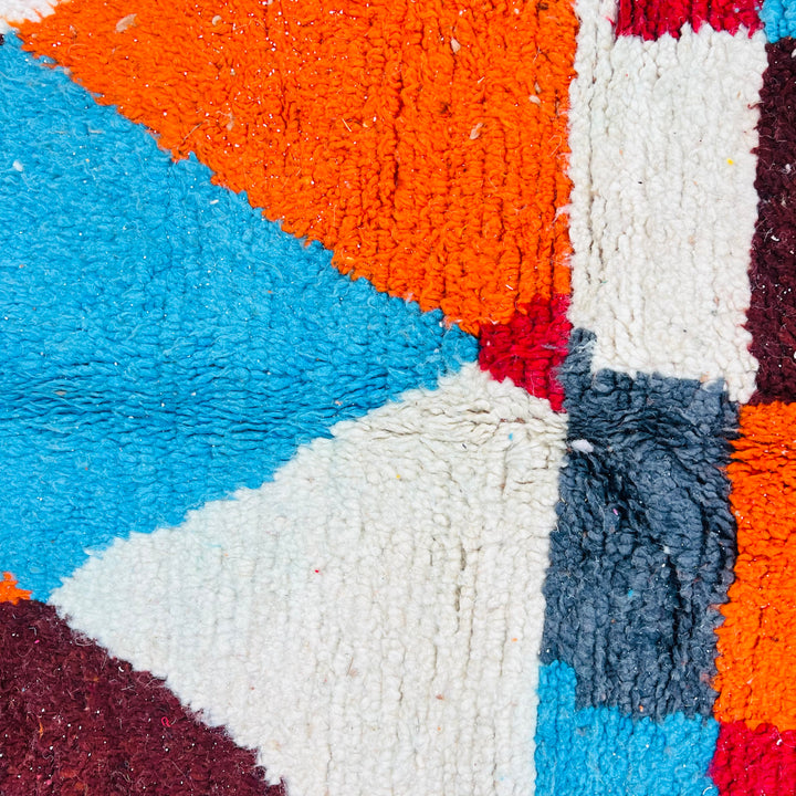 Close-up of a vintage Moroccan rug with bold geometric patterns in blue, orange, and cream, handcrafted using traditional Berber techniques.