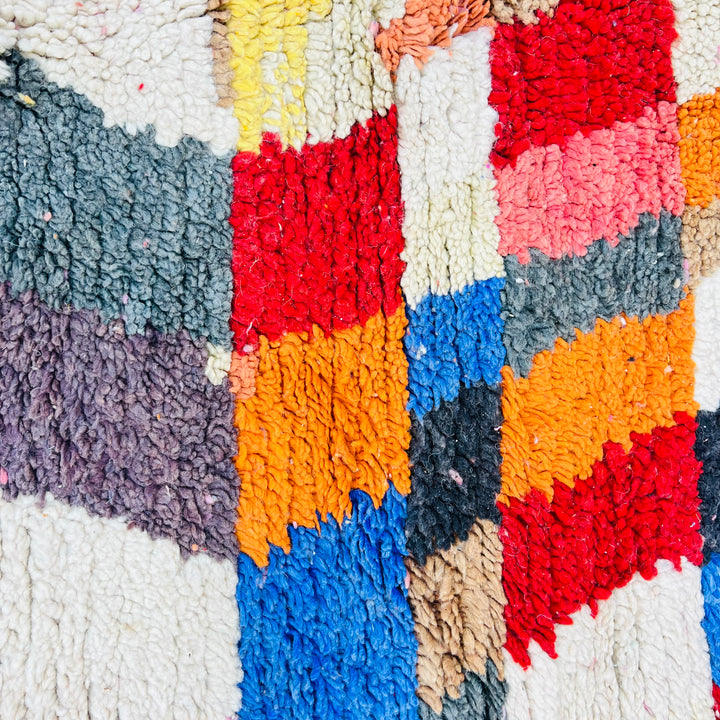 Colorful vintage Moroccan rug with geometric patterns in blue, red, yellow, and orange fibers, showcasing traditional Berber artistry.