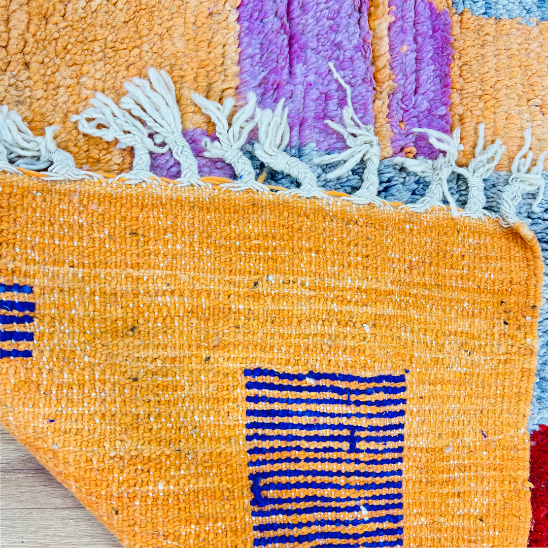Colorful Moroccan rug with fringe, showcasing vibrant geometric patterns in orange, purple, and blue, handmade with traditional techniques.