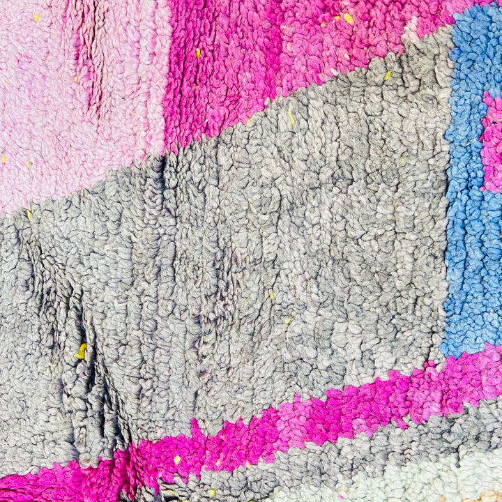 Close-up of a vintage Moroccan rug with vibrant pink, blue, and gray geometric patterns, handcrafted by Berber artisans.