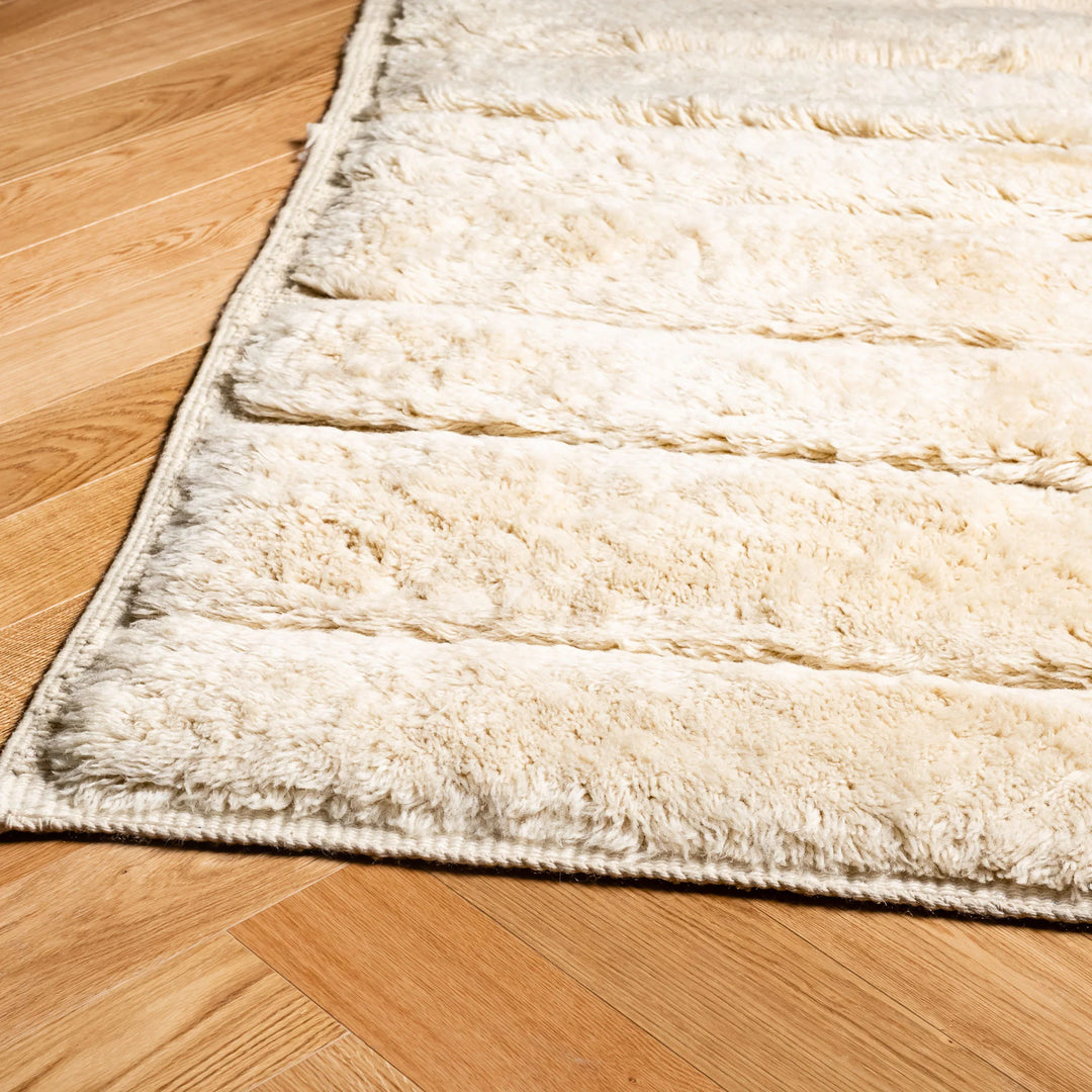 Ivory Beni Mrirt minimalist Moroccan wool rug on wooden floor, featuring subtle shaved lines and plush texture. Ideal for modern interiors.
