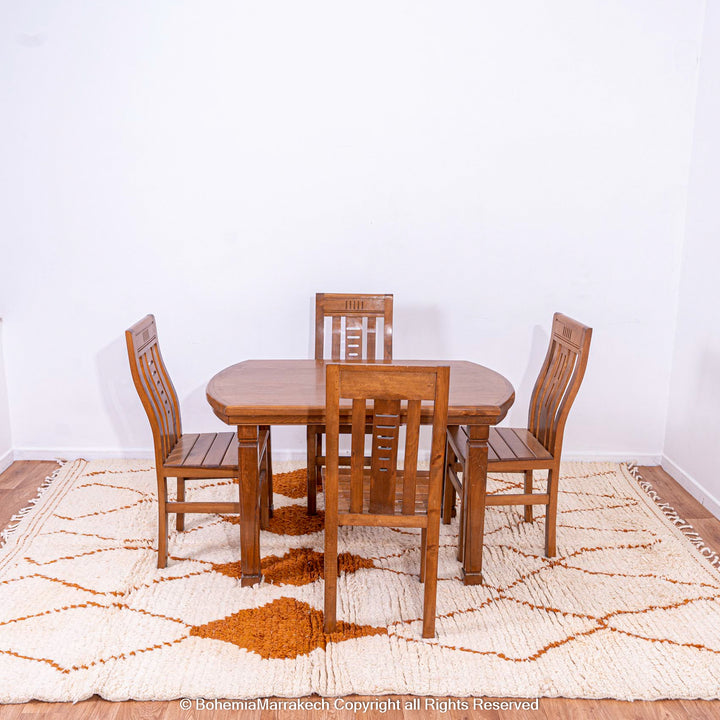 White Moroccan wool rug with rust diamond pattern under wooden dining table set, showcasing Berber craftsmanship.