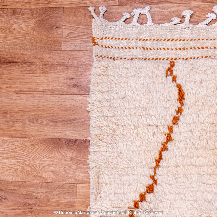 Handmade white Moroccan wool rug with rust diamond pattern on a wooden floor.