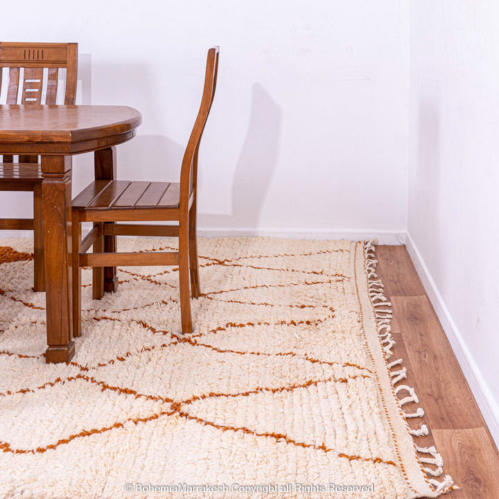 White Moroccan rug with rust diamonds in traditional Beni Ourain pattern, placed under a wooden dining set. Handmade wool rug.
