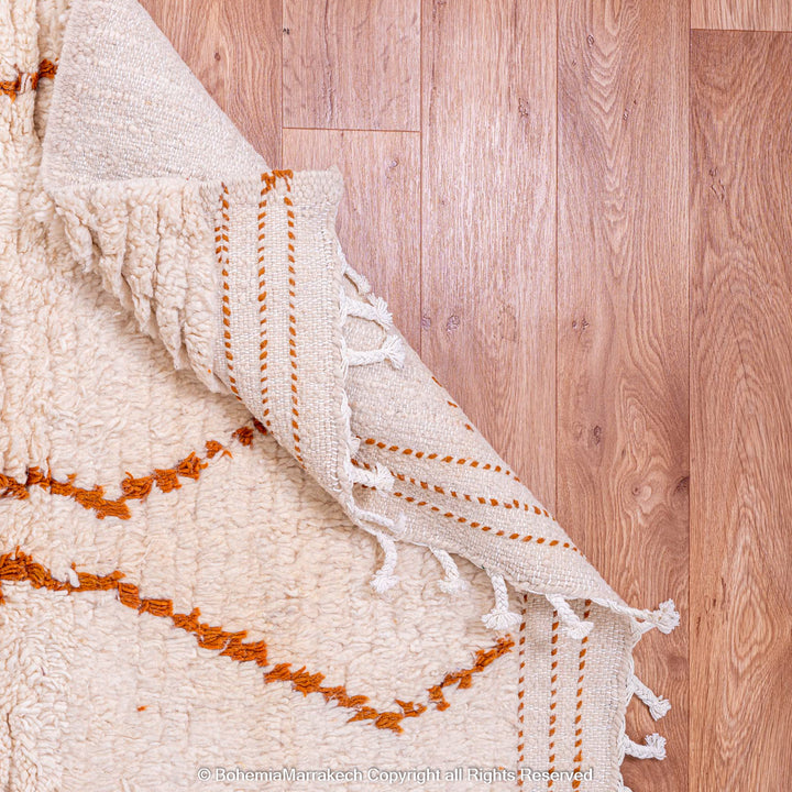 Handmade white Moroccan rug with rust diamond pattern on hardwood floor, crafted by Berber artisans with natural wool.