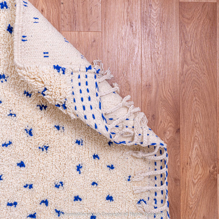 Large white Moroccan rug with blue dots, handwoven wool Beni Ourain, showcasing a traditional Moroccan pattern.