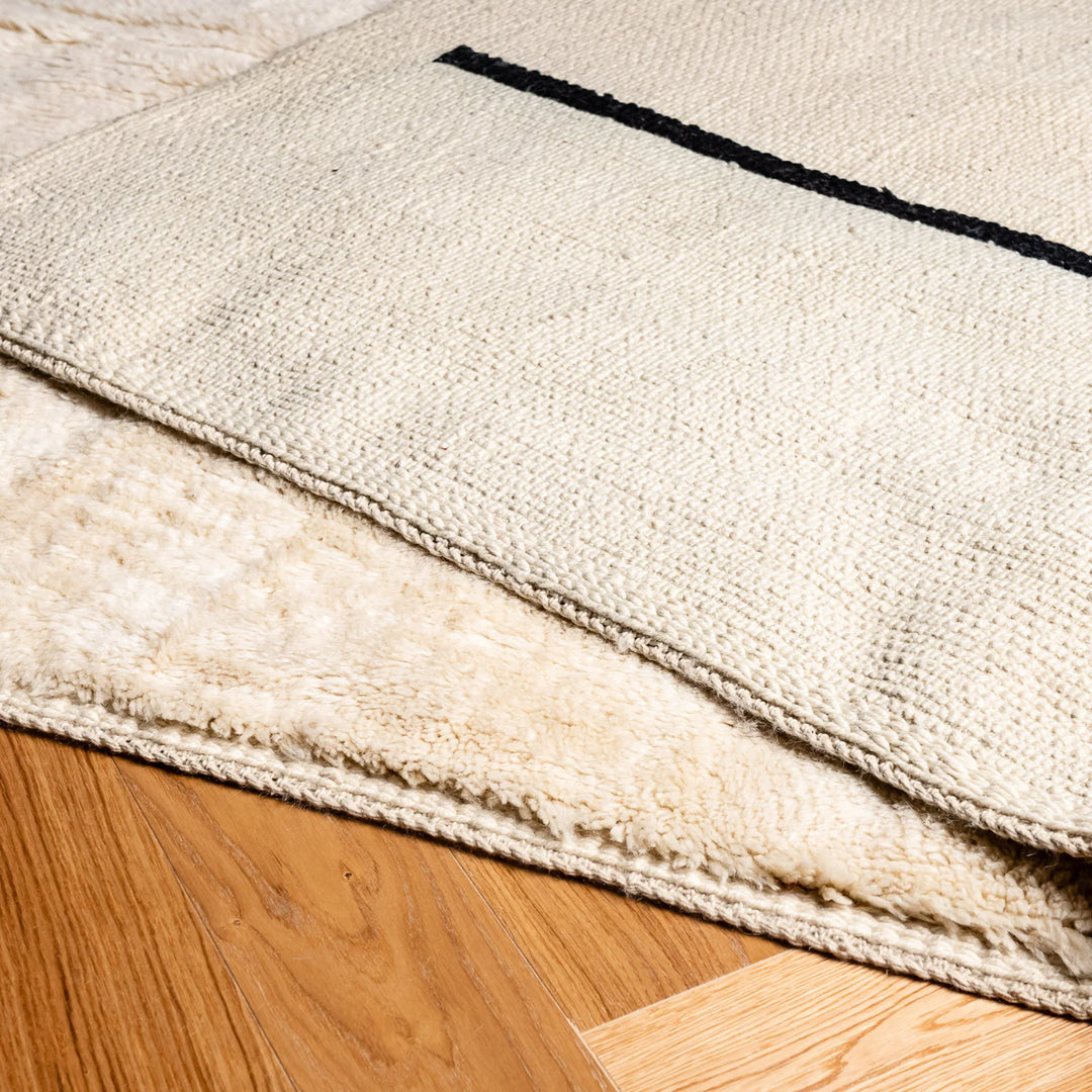 Minimalist Beni Ourain cream wool rug with black stripes, handmade Moroccan Berber style, soft and plush texture for modern interiors.