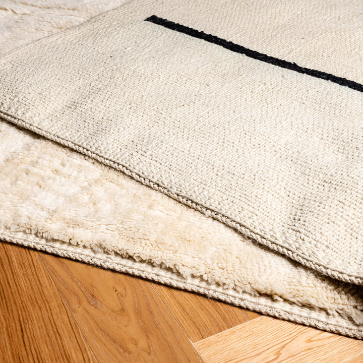 Minimalist Beni Ourain cream wool rug with black stripes, handmade Moroccan Berber style, soft and plush texture for modern interiors.