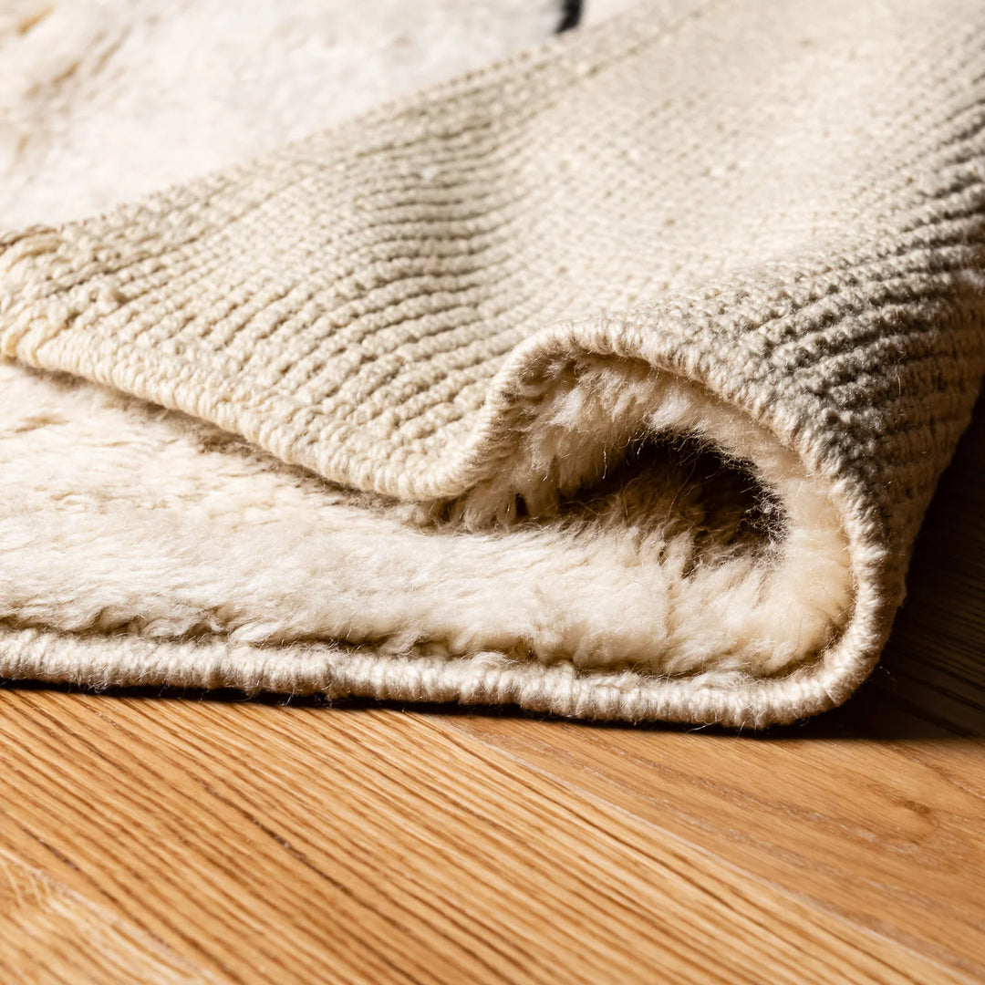 Close-up of a minimalist Beni Ourain cream rug with soft wool and black stripes, showcasing its plush texture on a wooden floor.
