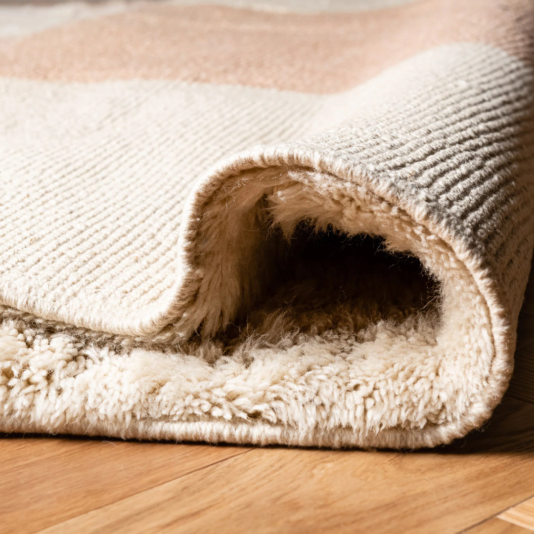 Close-up of a minimalist Moroccan wool rug with peach stripes on a creamy texture, perfect for cozy living spaces.