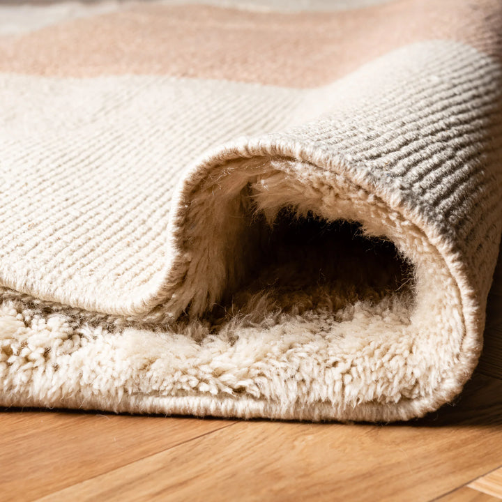 Close-up of a minimalist Moroccan wool rug with peach stripes on a creamy texture, perfect for cozy living spaces.