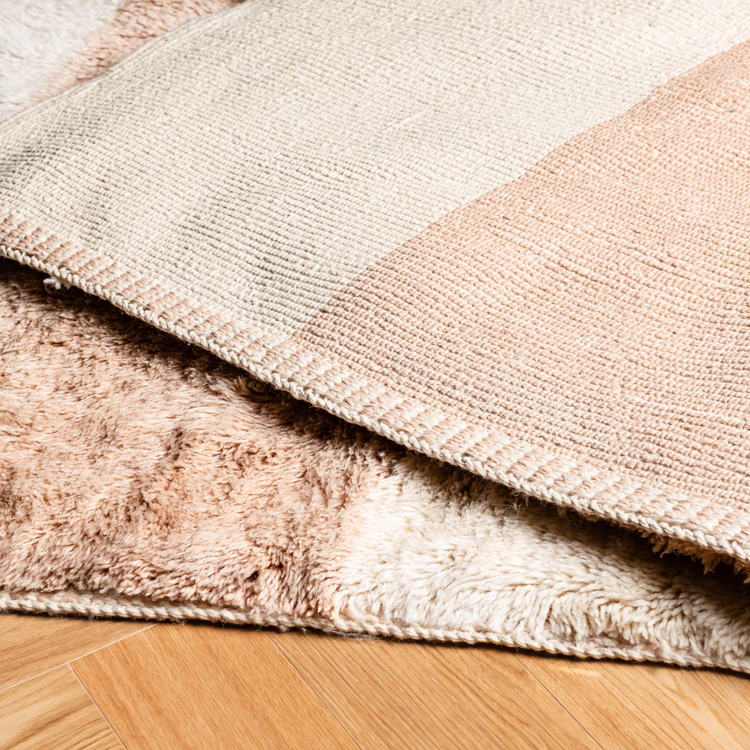 Minimalist Moroccan wool rug with peach stripes, showcasing intricate handwoven texture on wooden floor. Perfect for bedrooms and living spaces.