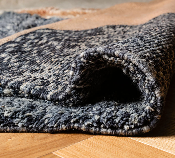 Close-up view of a modern abstract Moroccan rug, showcasing intricate geometric patterns in natural wool with soft shades of charcoal and ivory.