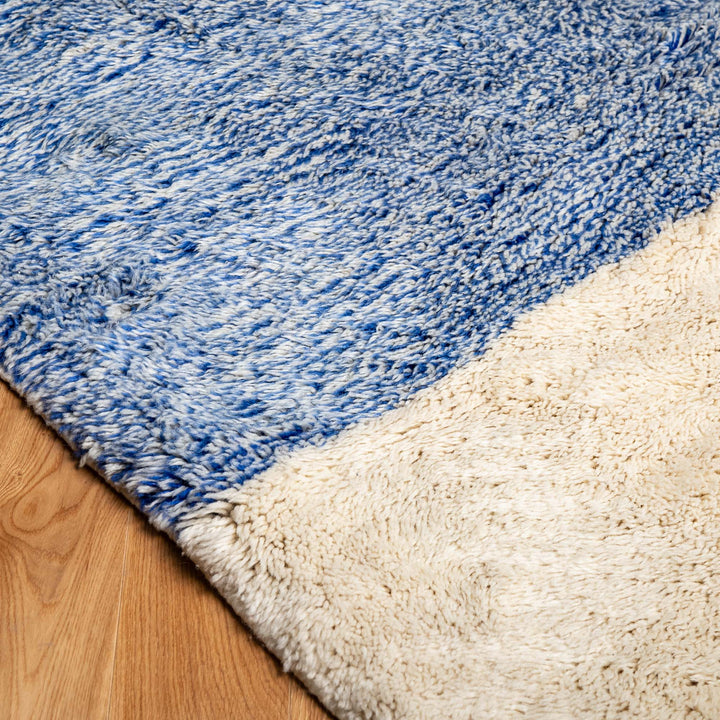 Blue and cream wool Moroccan rug on wooden floor, showcasing textured pattern and vibrant colors for modern interiors.