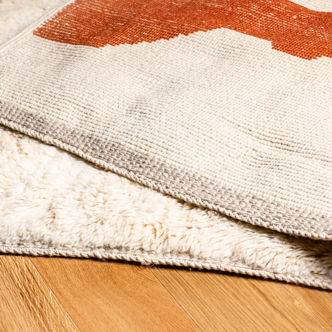 Close-up of a modern abstract Moroccan wool rug in terracotta and beige, showcasing plush texture on wooden floor.