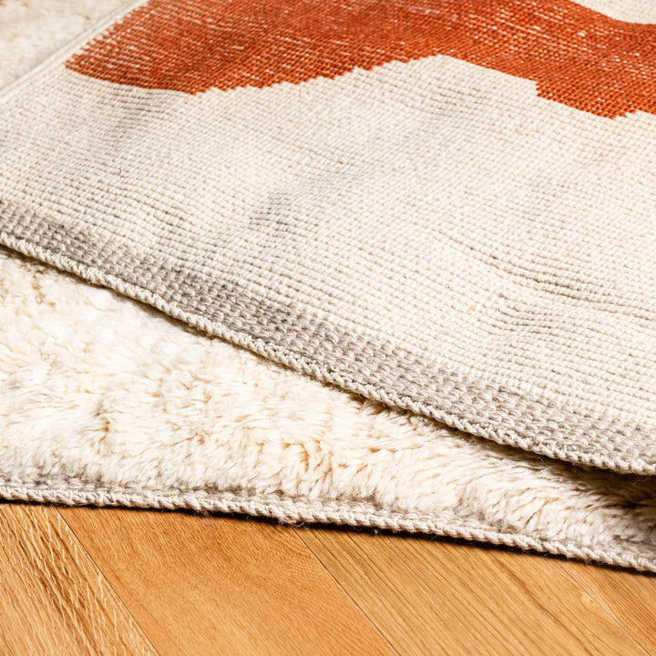 Close-up of a modern abstract Moroccan wool rug in terracotta and beige, showcasing plush texture on wooden floor.