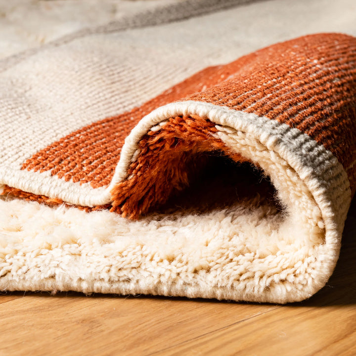 Close-up of a folded modern abstract Moroccan wool rug in terracotta and beige, showing its plush texture and detailed craftsmanship.