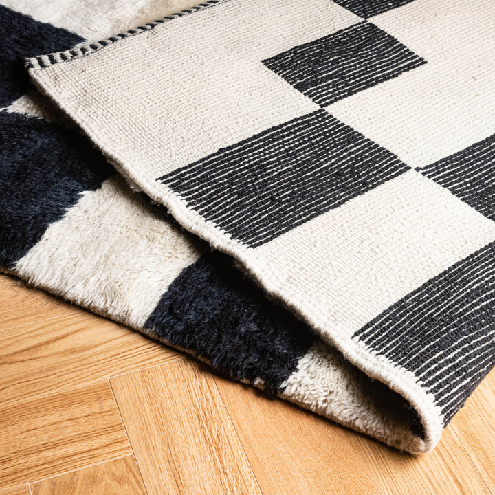 Modern Beni Mrirt black and ivory checkerboard wool rug from Morocco on wooden floor, showcasing intricate handwoven patterns.