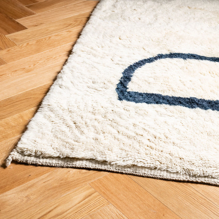 Modern Beni Mrirt Moroccan wool rug with black abstract lines, hand-knotted design on creamy white background on wood floor.