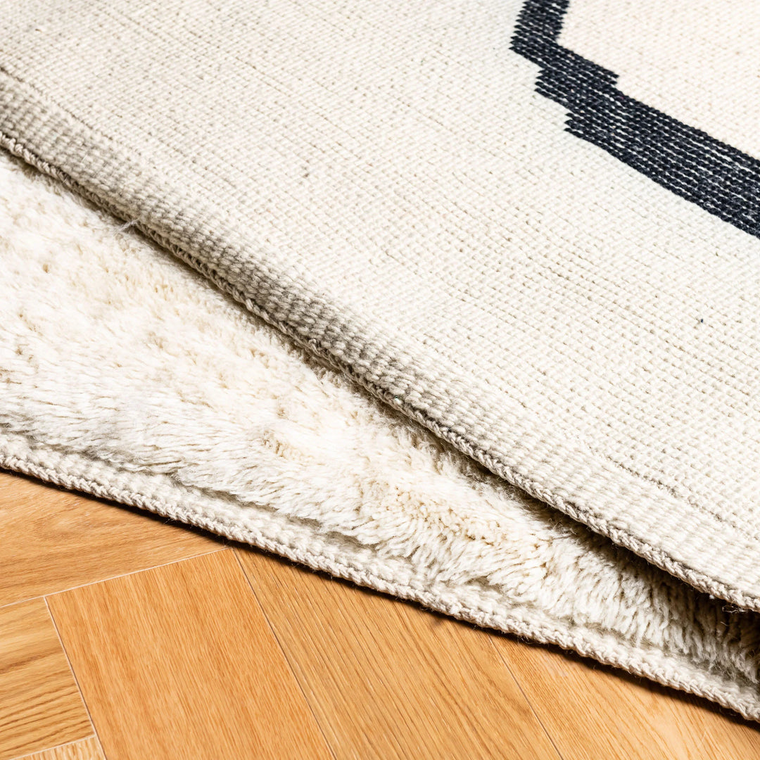 Modern Beni Mrirt wool rug with black abstract lines, handcrafted in Morocco, displaying texture on hardwood floor.