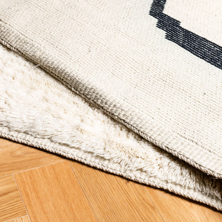 Modern Beni Mrirt wool rug with black abstract lines, handcrafted in Morocco, displaying texture on hardwood floor.
